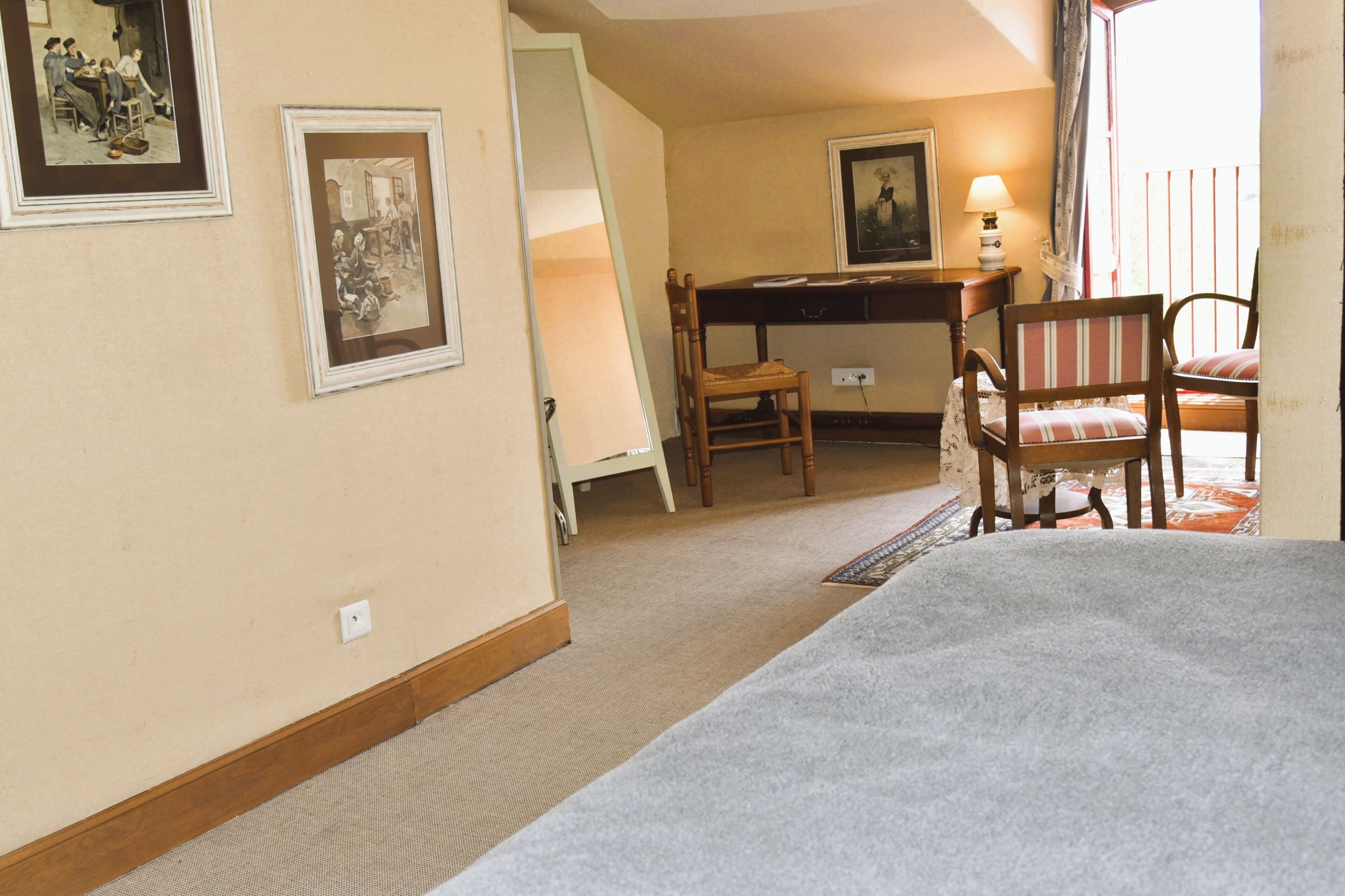 Habitació d'hotel amb un llit, una taula de treball, dues cadires, una làmpada i quadres a la paret.