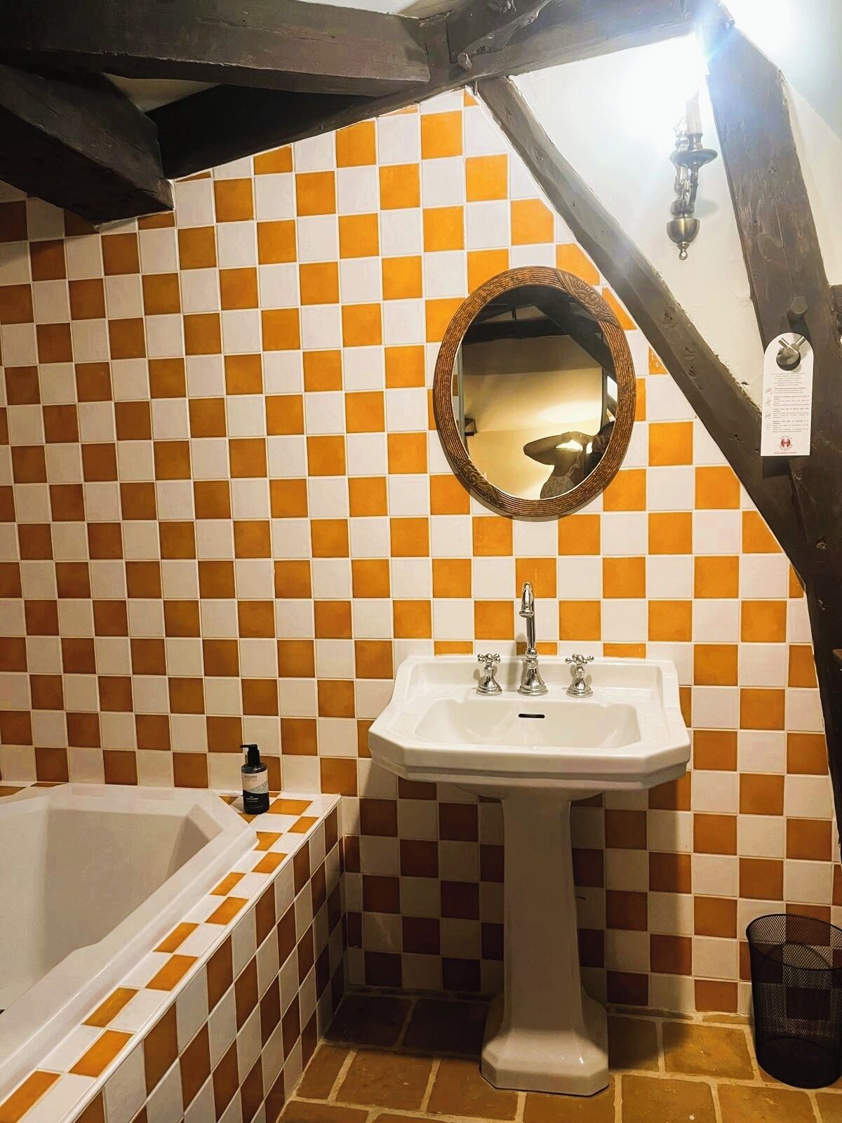 Une salle de bain avec un mur recouvert de carreaux à motifs, un lavabo blanc, un miroir et une baignoire.