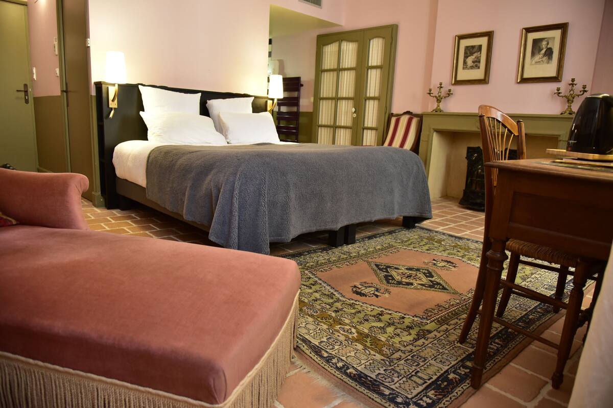 Een slaapkamer met een bed, een stoel, een tafel en een kamerbreed tapijt met een patroon.