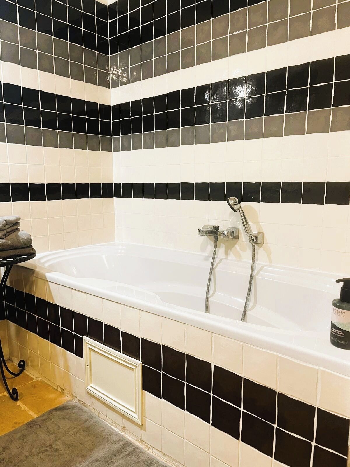 Une salle de bain avec une baignoire, des carreaux noirs et blancs, un porte-serviettes et une bouteille de shampoing.