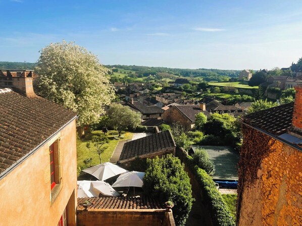 A view of a village with traditional architecture, a river, and a large tree. - Logis Hôtel Le Boudoir (Pays-de-Belves)