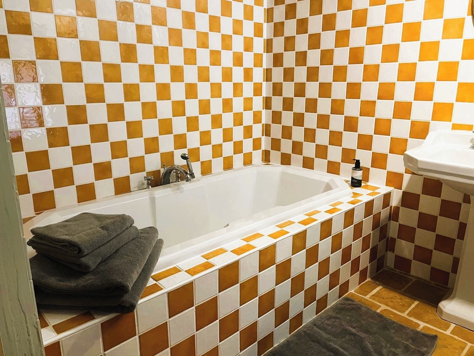 Une salle de bain avec un carrelage à motifs à carreaux, une baignoire blanche, un lavabo et une pile de serviettes.