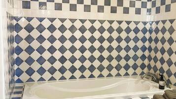 A bathroom with a checkered tile wall, a bathtub, and a small trash bin.