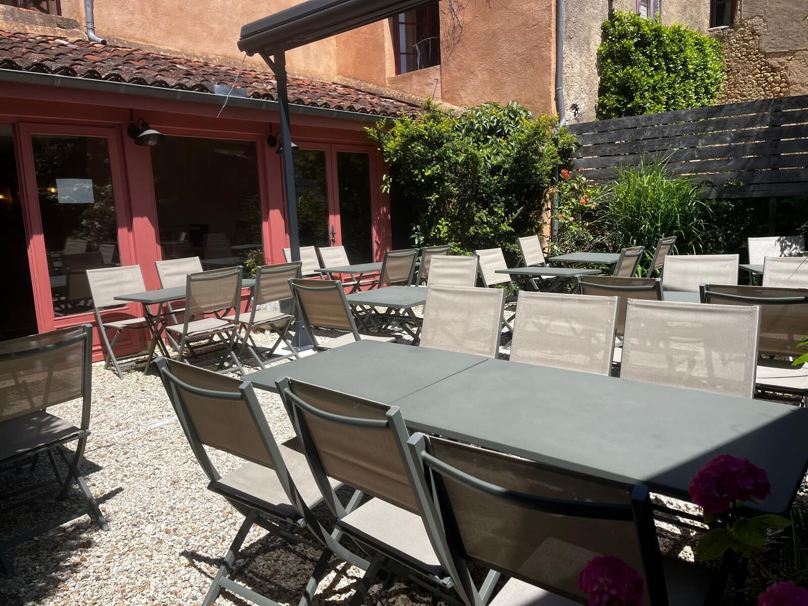 An outdoor patio with tables and chairs, a red building, and greenery.