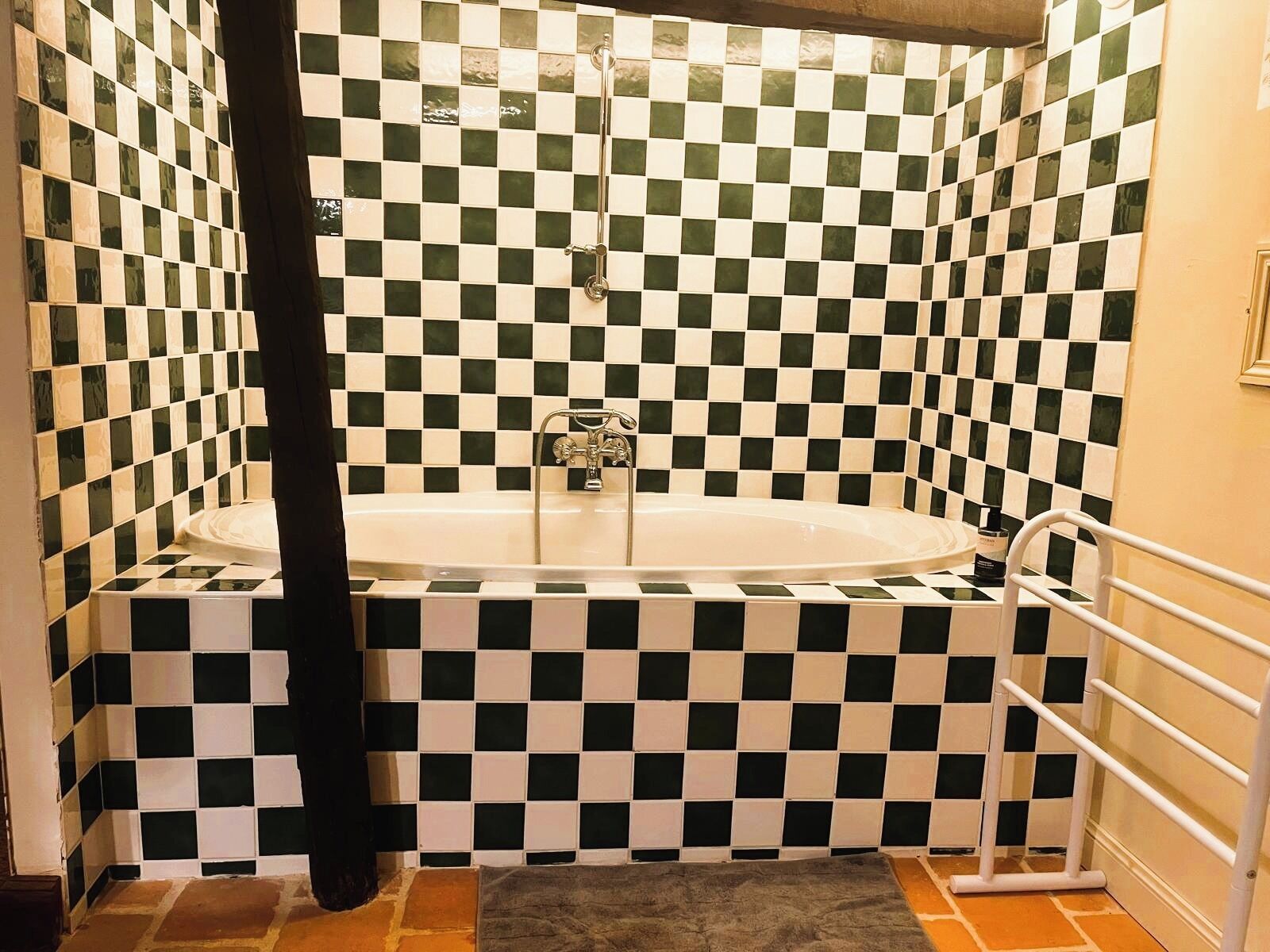 A bathroom with a checkered tile wall, a bathtub, and a shower area.