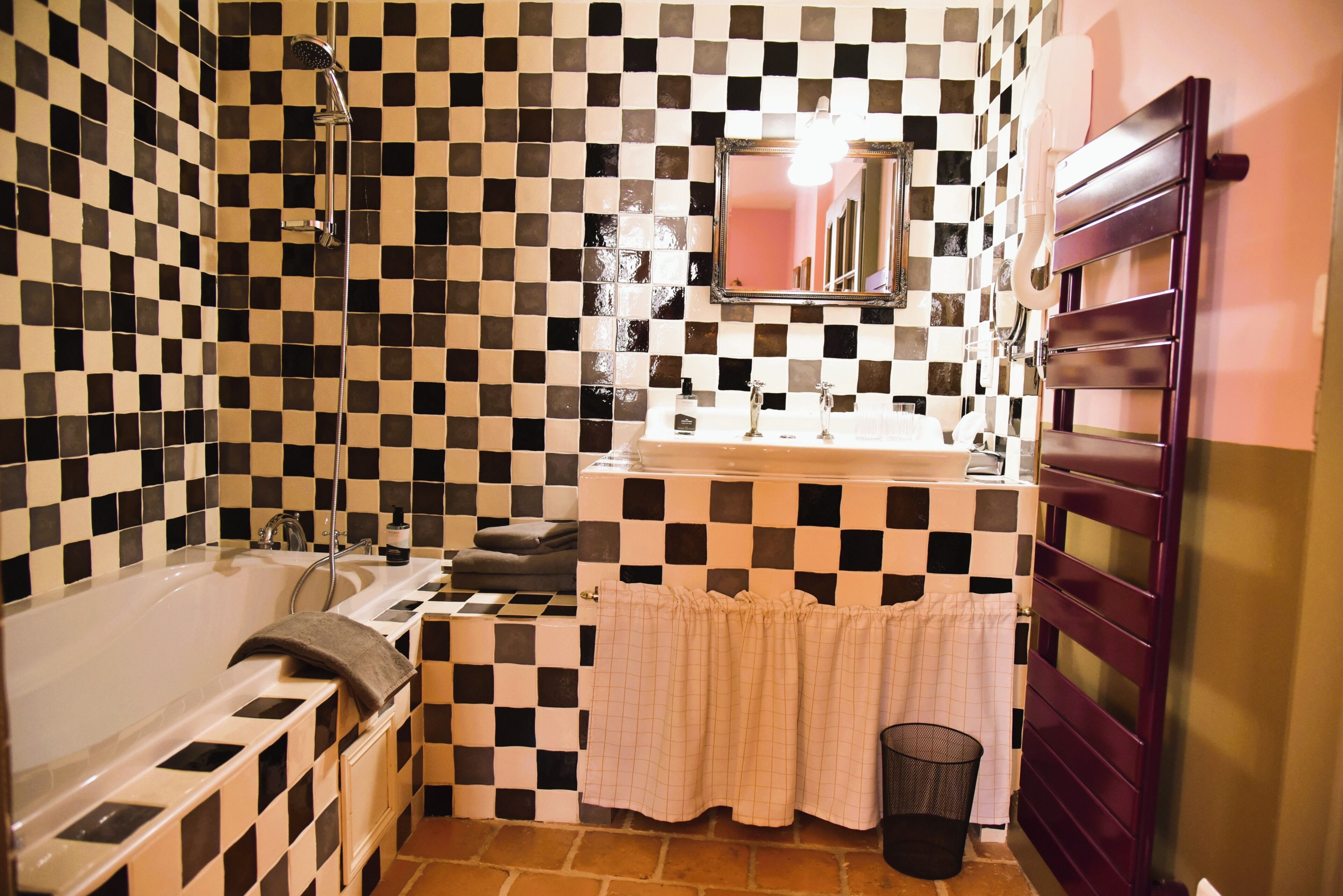 A bathroom with a checkered tile wall, a bathtub, a sink with a mirror, and a towel rack.