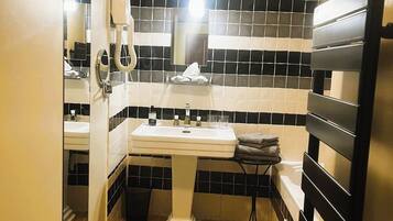 Un baño con un lavamanos blanco pedestal, paredes con azulejos blanco y negro, un perchero negro y un pequeño cubo de basura.