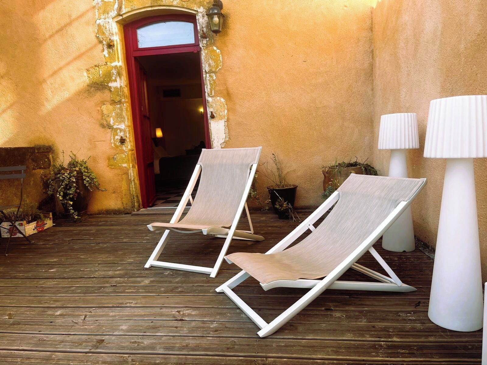 Two lounge chairs on a wooden deck, a red door, and two white lamps.