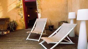 Two lounge chairs on a wooden deck, a red door, and two white lamps.