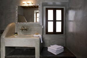 A bathroom with a freestanding bathtub, a mirror with a decorative frame, and a window with a wooden frame. - CasaLindos (Rhodes)