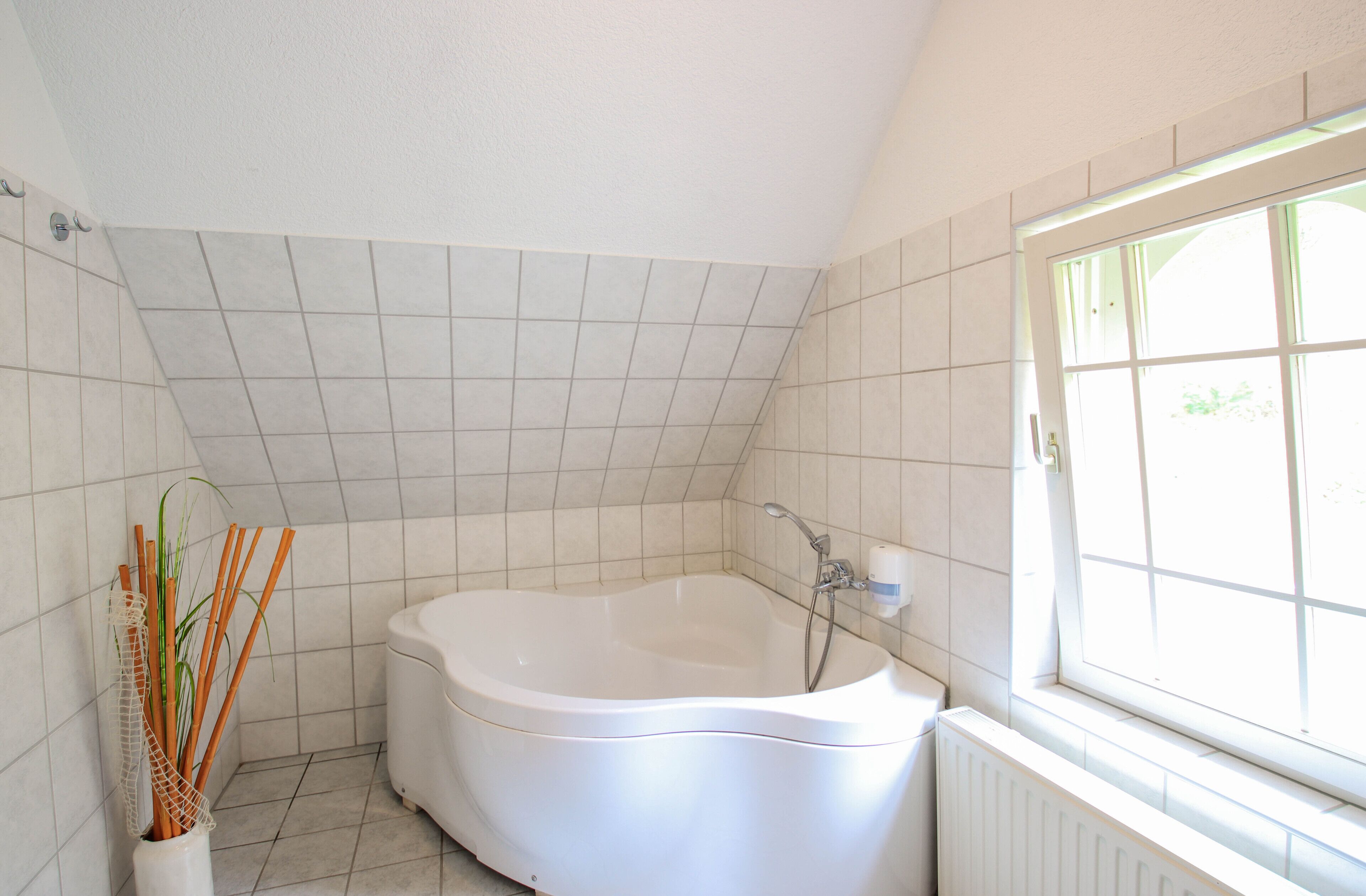 A modern bathroom with a freestanding bathtub, tiled walls, and a window providing natural light.