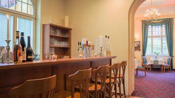 A bar area with wooden chairs, shelves with glasses and bottles, and a view of a dining area with a table and chairs.