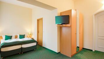 Una habitación de hotel con una cama, un televisor montado en un mueble de madera y una puerta que da a otra habitación.
