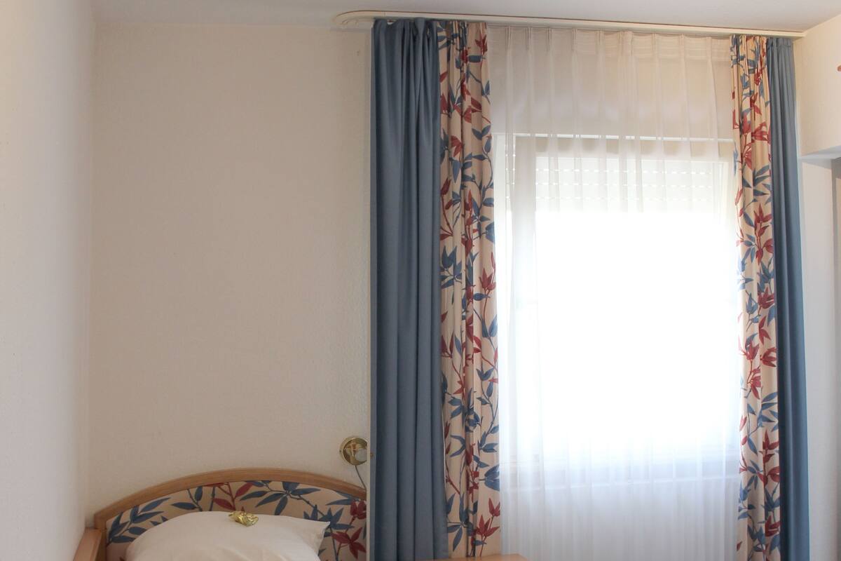 A single bed with a wooden headboard, a small wooden nightstand, and a blue carpeted floor.