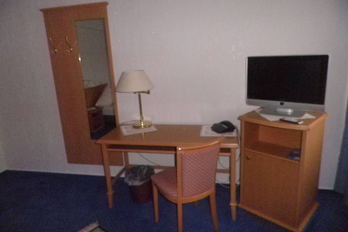 A small room with a desk, chair, lamp, television, and a mirror.