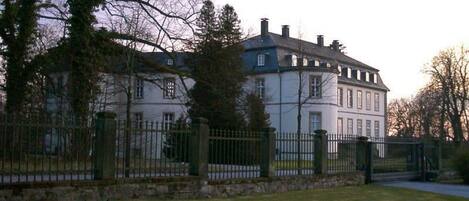 Un grand bâtiment à deux étages, doté d’une façade symétrique, d’une entrée centrale et entouré d’un mur de pierre.