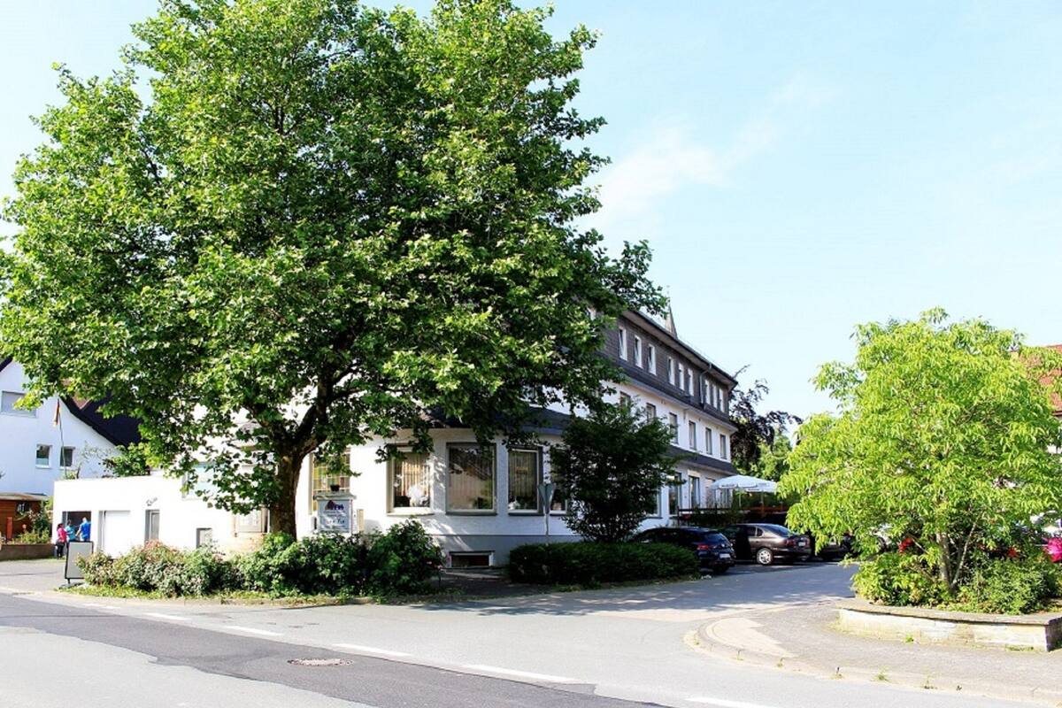 A two-story building with a large tree in front, parked cars, and a clear sky.
