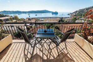 A balcony with a table and chairs, overlooking a harbor with boats and a ship.