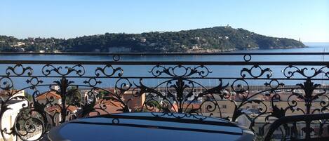 A terrace with a table and chairs, overlooking a body of water and a distant hill.