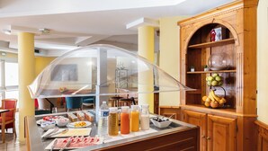 Un espace buffet proposant une variété de plats et de boissons, un buffet en bois garni de fruits et une vitrine en verre recouvrant le buffet.