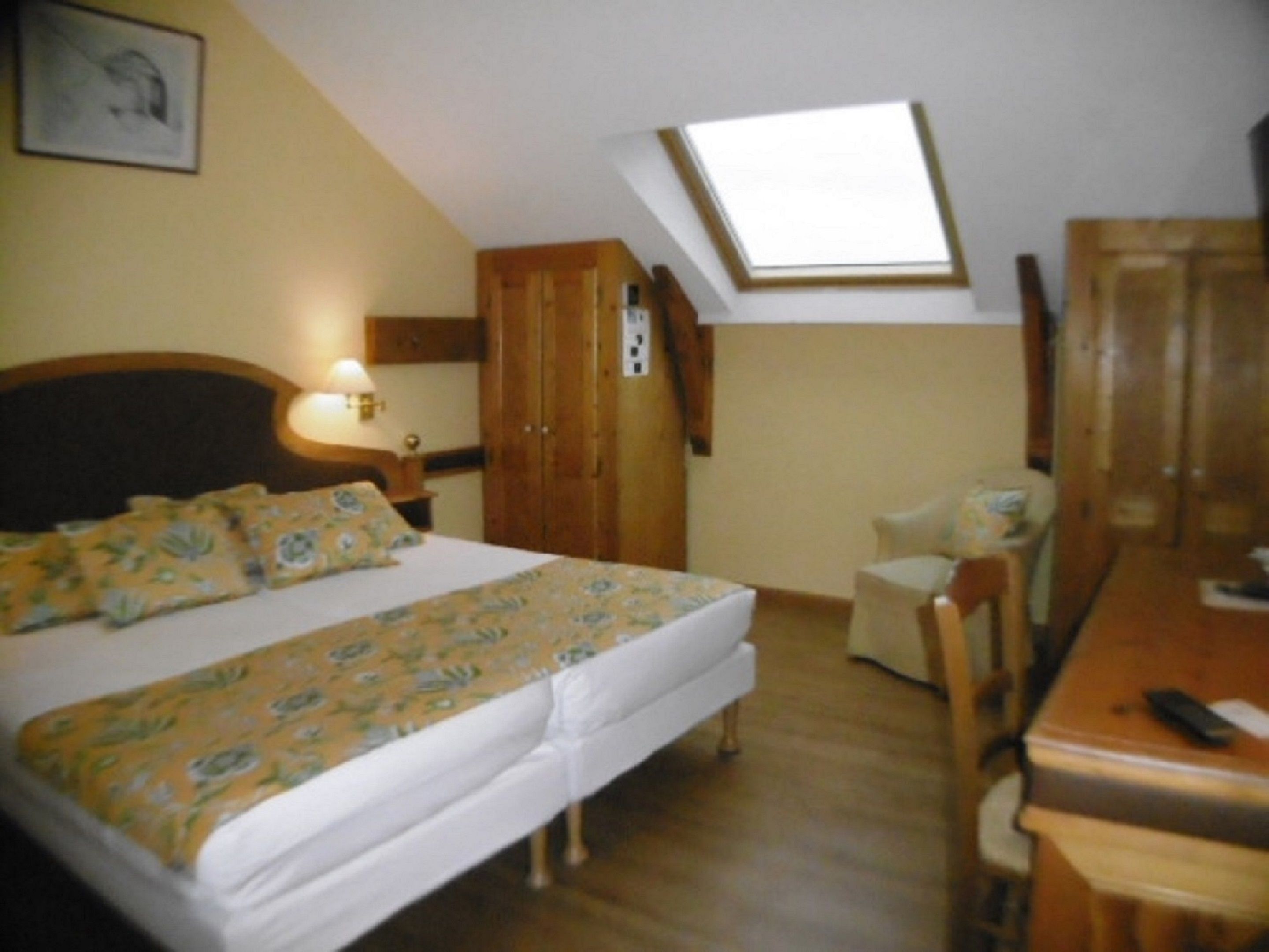 Un dormitorio con cama, escritorio, silla, armario y tragaluz.