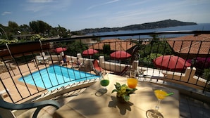 Un balcon avec une piscine, des parasols rouges et une table avec des boissons et une plante.