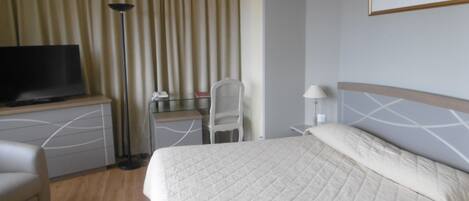Quarto de hotel com cama, escrivaninha, cadeira, televisão e um quadro na parede.