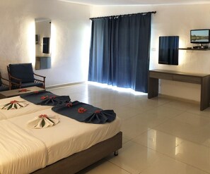 A hotel room with a bed, a desk, a chair, a TV, and a large window with curtains.