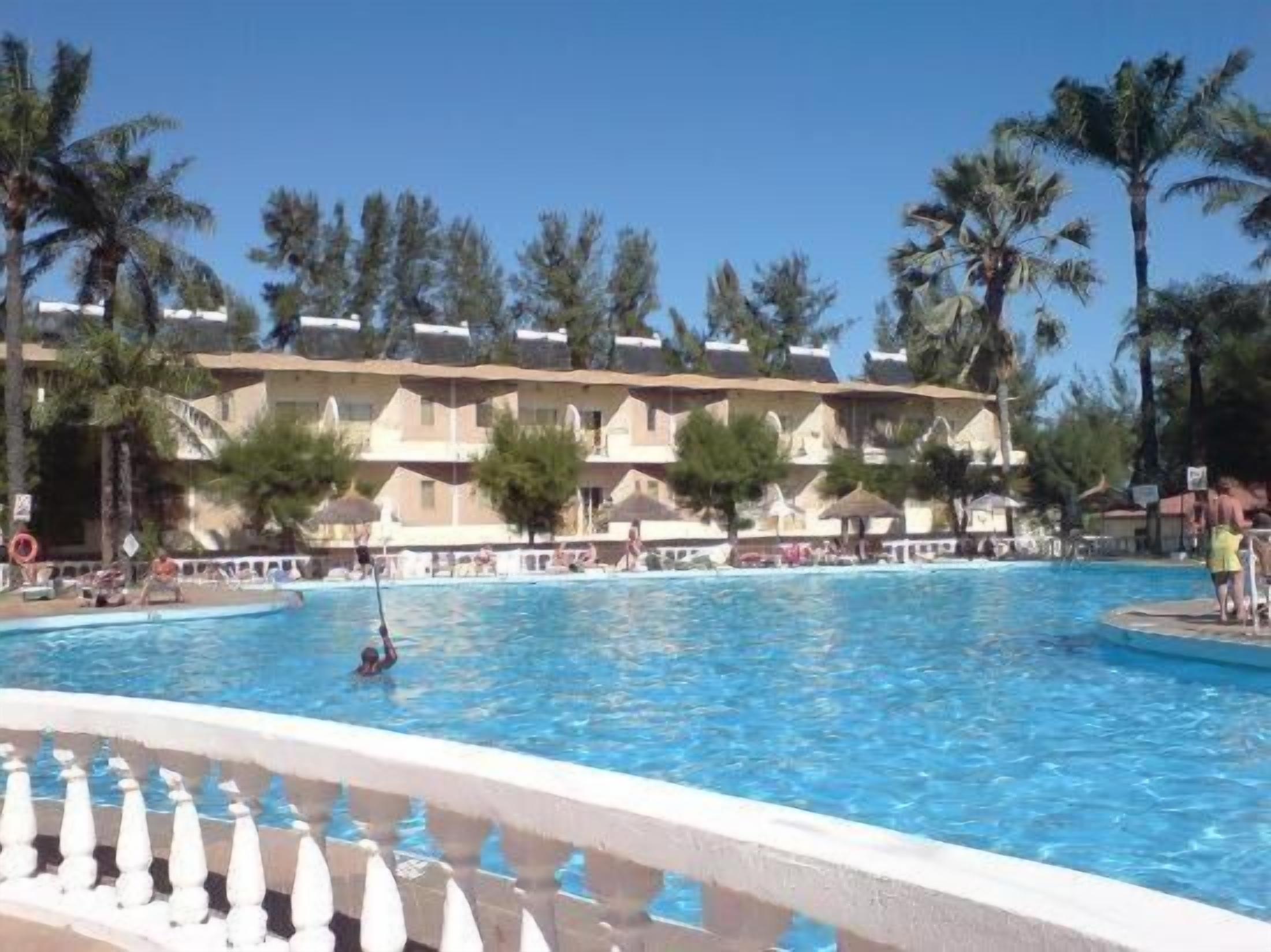 Un hotel con una piscina grande, palmeras y un cielo azul despejado.