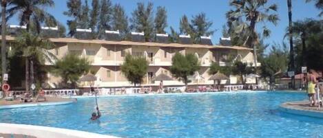 Un hotel con una piscina grande, palmeras y un cielo azul despejado.