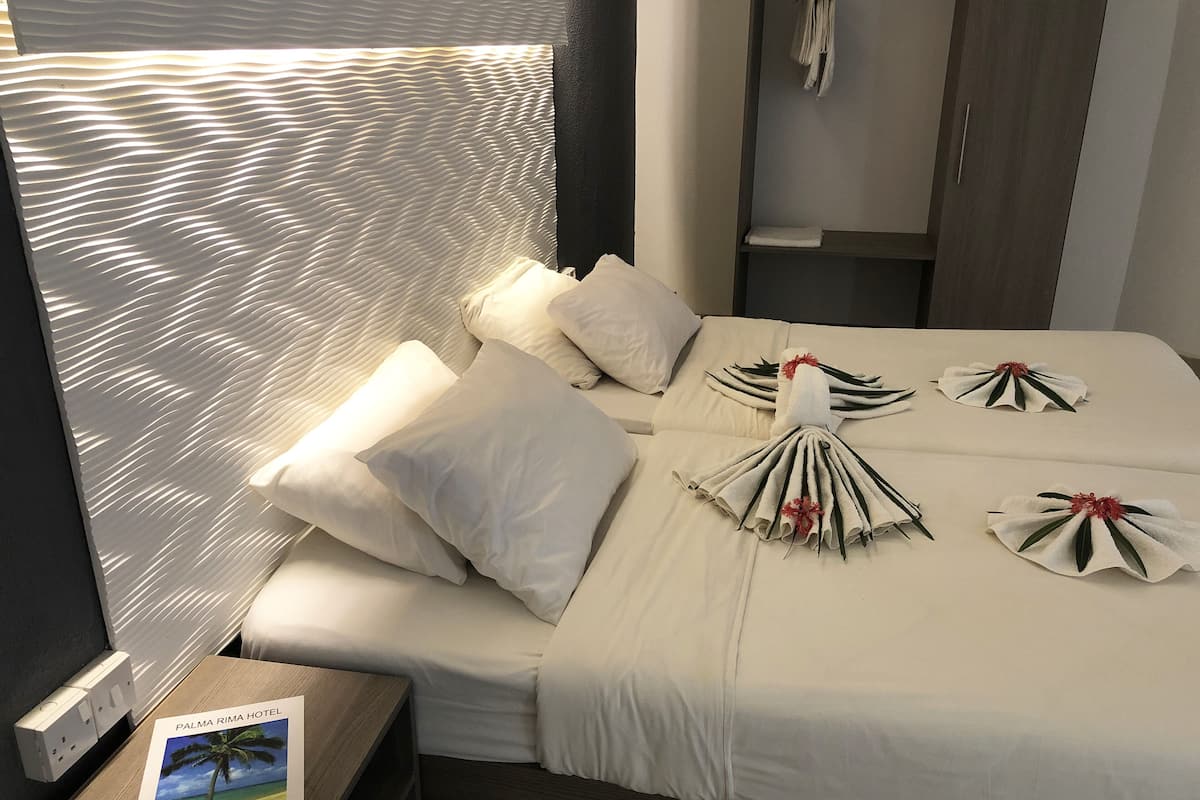 A hotel room with a neatly made bed, a nightstand with a welcome card, and a window with a textured blind.