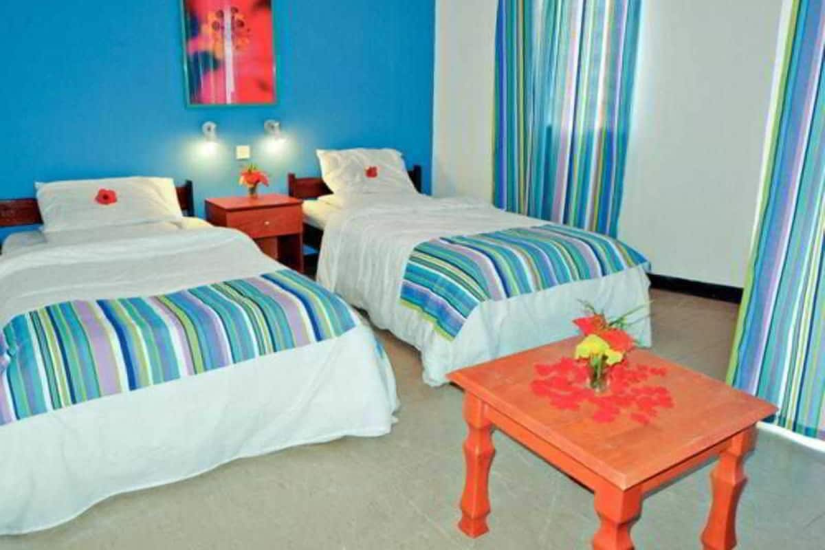 A hotel room with two beds, a small table with a vase of flowers, and a colorful striped curtain.