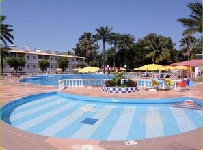 A swimming pool with a checkered pattern, surrounded by palm trees and umbrellas.