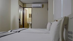Une chambre d’hôtel avec deux lits, une salle de bain avec un lavabo et un appareil de climatisation fixé au mur.