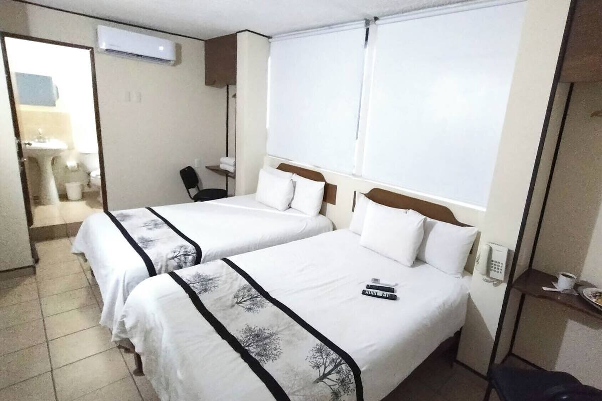 A hotel room with two beds, a desk, a chair, a telephone, and a small table with a plate and cup.