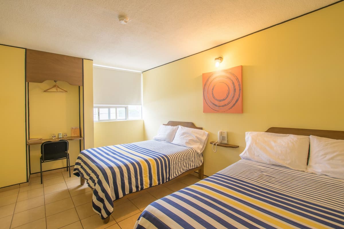 A hotel room with two beds, a desk, a chair, a phone, and a wall with a circular design.