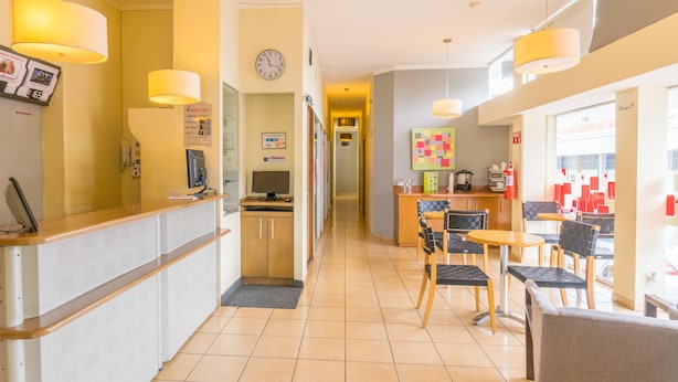 Un hall d’hôtel comprenant un comptoir d’accueil, une horloge, un espace où l’on peut se servir du café et un coin salon.