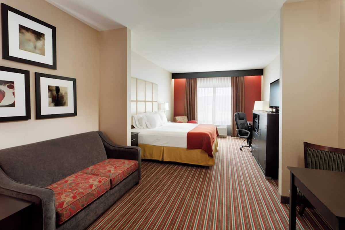 A hotel room with a bed, a sofa, a desk, and a TV.