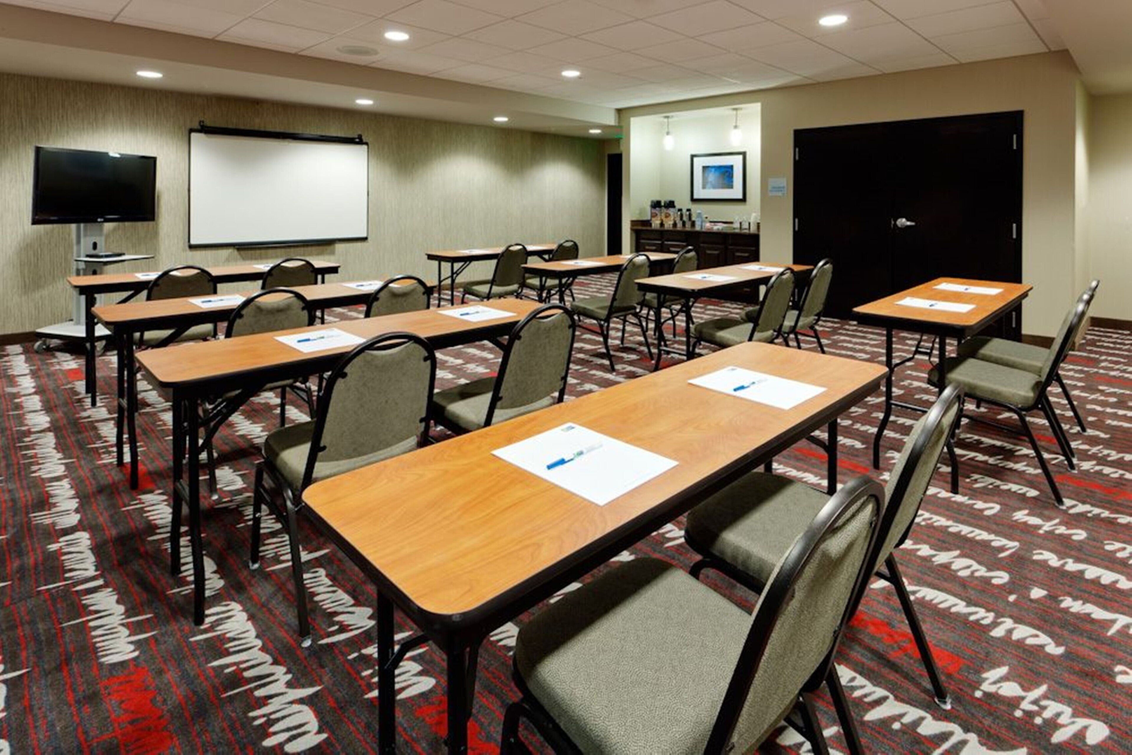 Un salón de conferencias con varias mesas y sillas, una pantalla de proyección y una puerta.