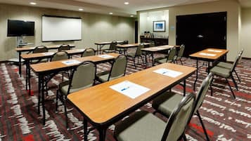 Un salón de conferencias con varias mesas y sillas, una pantalla de proyección y una puerta.