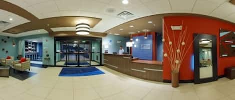 A hotel lobby with a reception desk, seating area, and a glass door entrance.