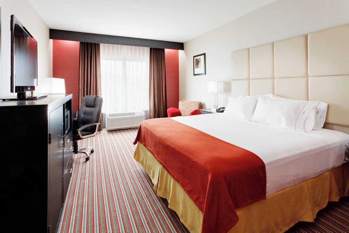 A hotel room with a large bed, a desk with a computer, a chair, a television, and a window with curtains.