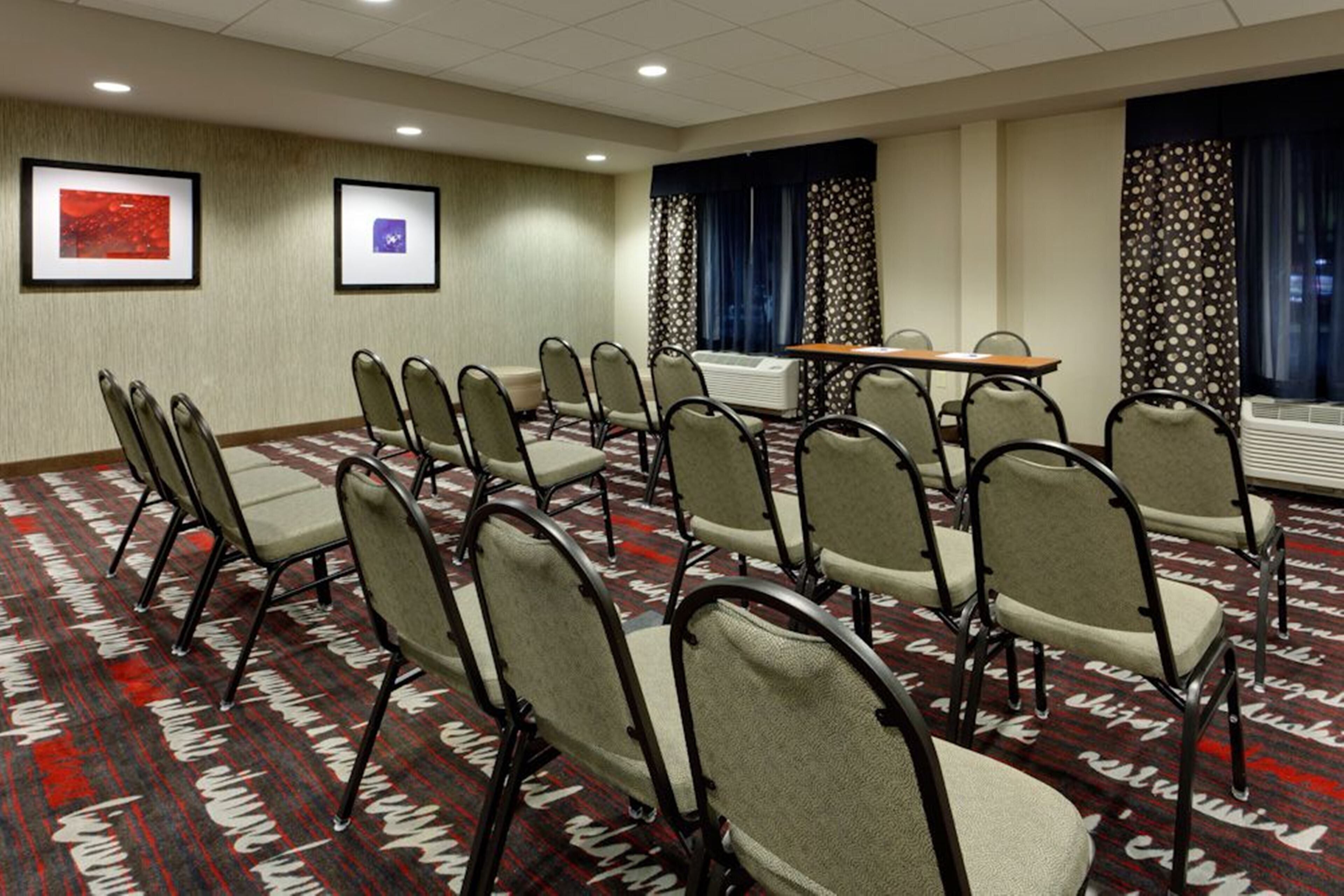 A conference room with rows of chairs, a table, and two framed pictures on the wall.