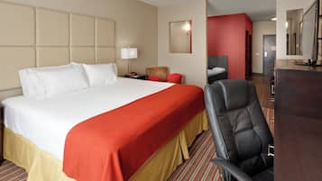 A hotel room with a large bed, a desk, a chair, and a mirror.