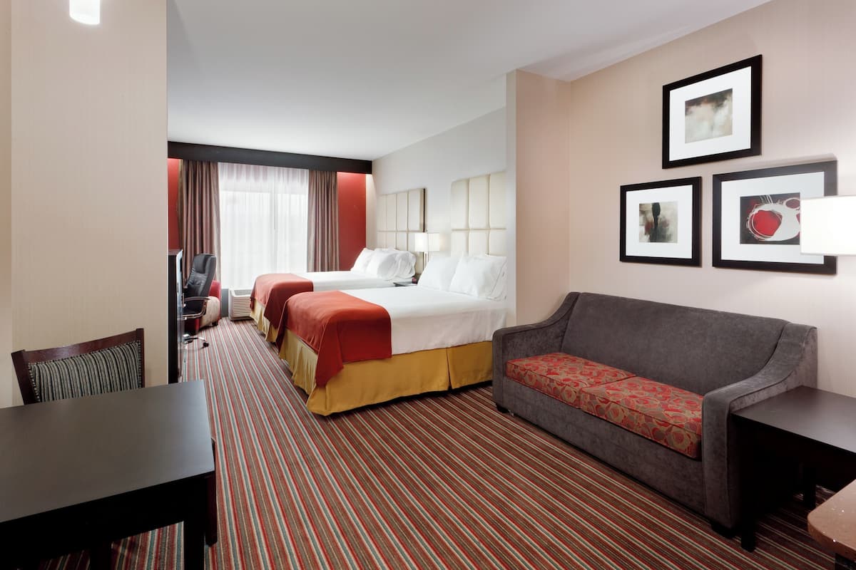 A hotel room with a bed, a sofa, a dining table, and a chair. There are framed pictures on the wall.