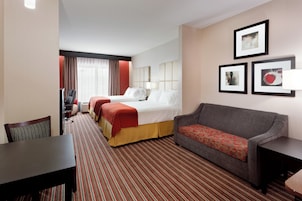 Habitación de hotel con cama, sofá, mesa de comedor y una silla. En la pared, hay cuadros enmarcados.