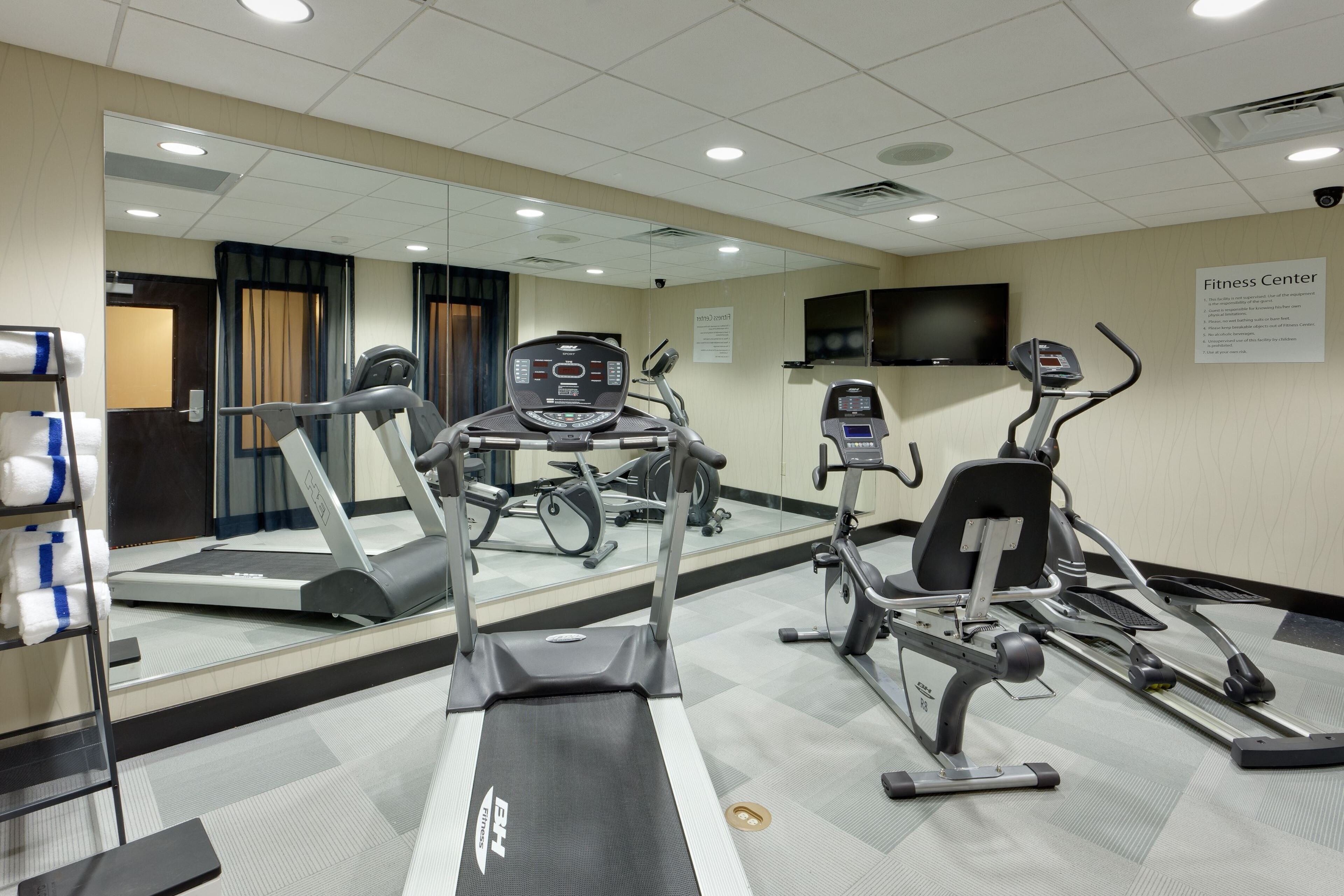 A fitness center with treadmills, elliptical machines, and a mirrored wall.