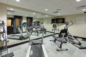 Un gimnasio equipado con cintas de correr, elípticas y un espejo grande.