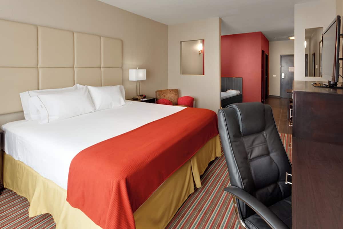 A hotel room with a large bed, a desk, a chair, a mirror, and a red accent wall.