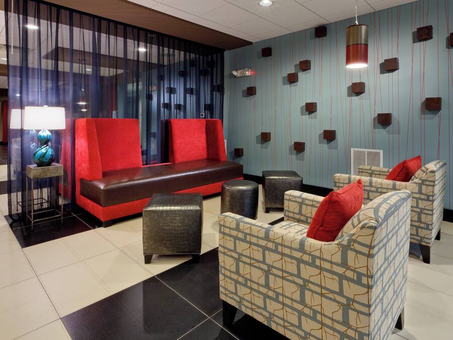 A lobby with a red sofa, patterned armchairs, and a decorative wall with vertical lines and cube-shaped elements.